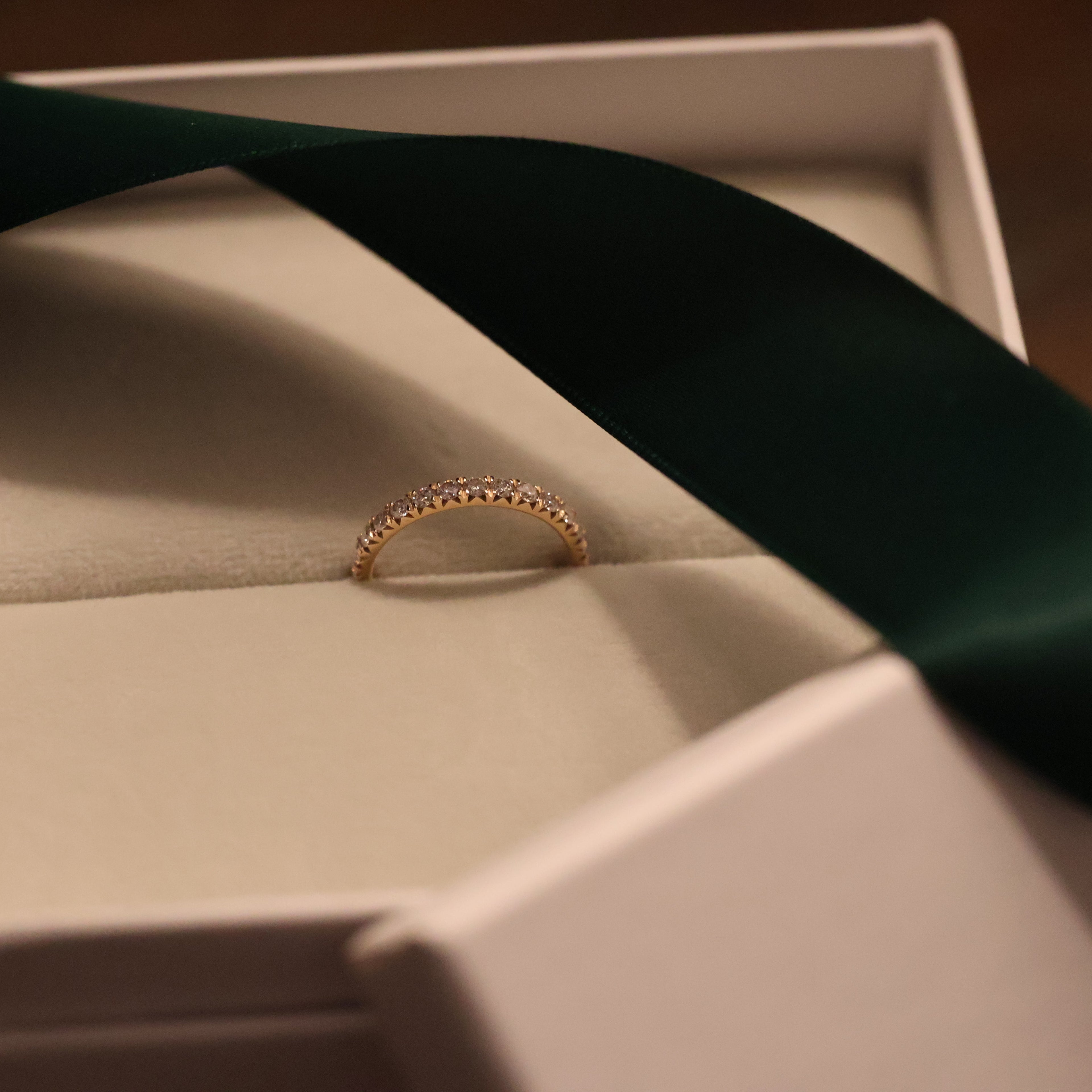 Gold diamond half eternity band in an open box with a green ribbon