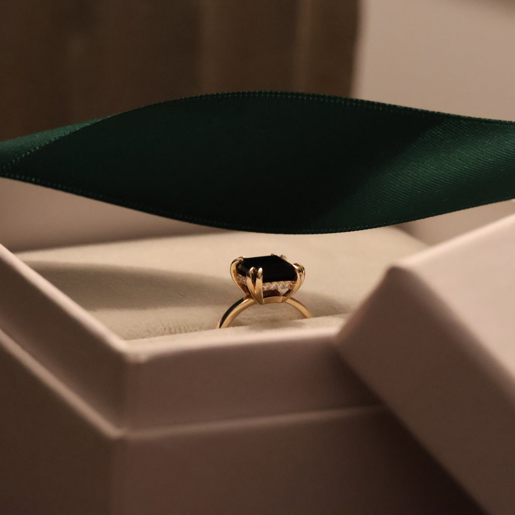 Gold ring with a black onyx gemstone in a white box with a green ribbon