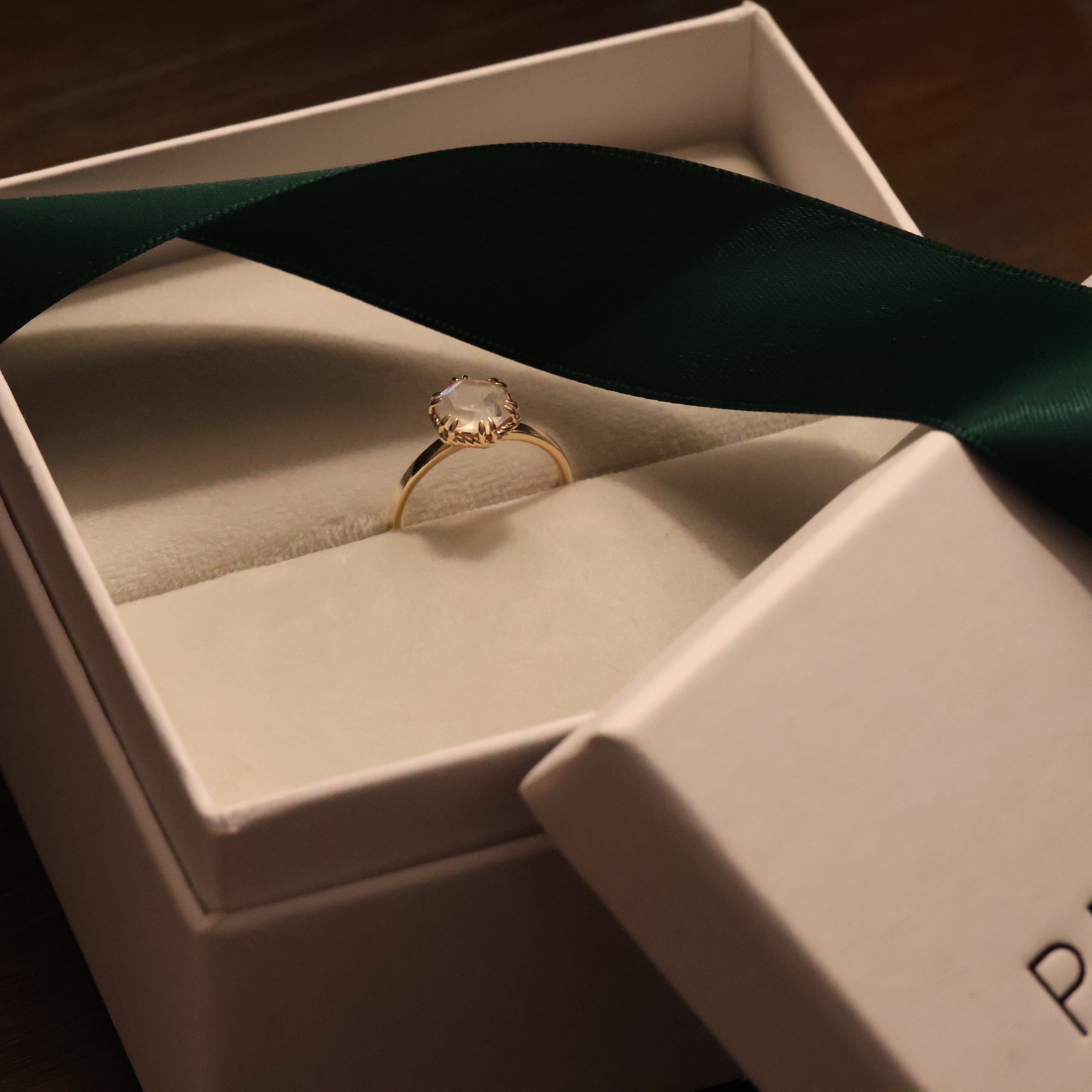 Gold ring with hexagon moonstone  in a Periana jewelry box with a green ribbon
